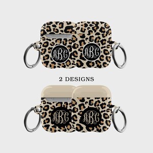 Puede incluir: Dos diseños de fundas para Airpods con estampado de leopardo y un círculo negro con las letras ABC en blanco. Las fundas tienen un anillo plateado.