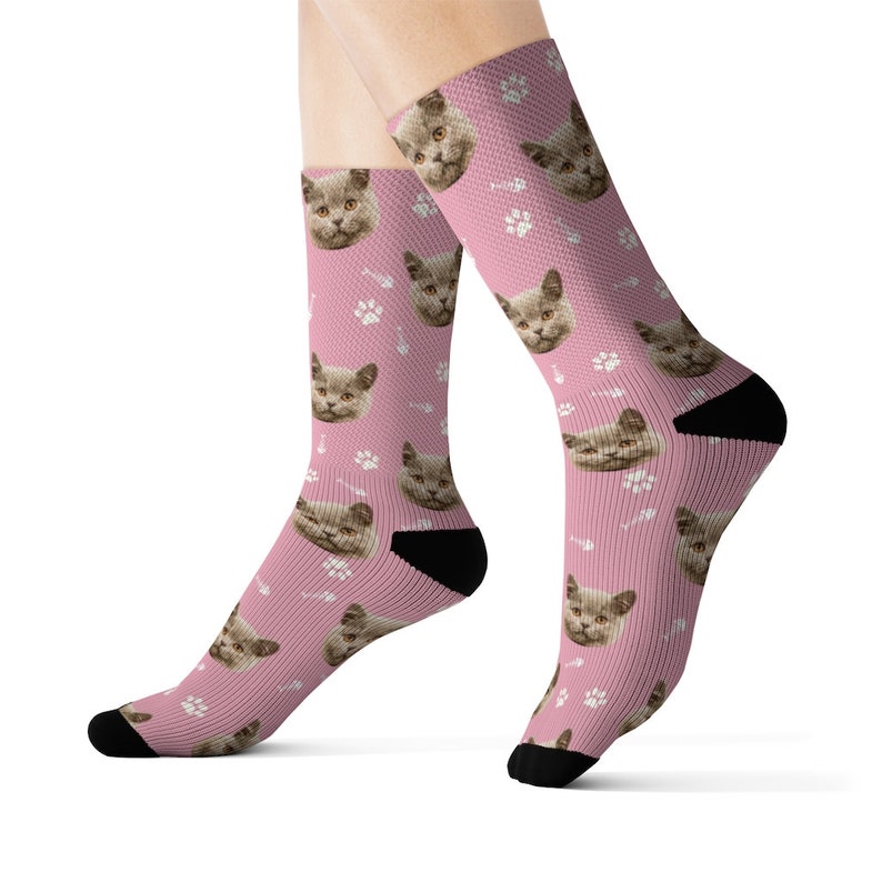 May include: A pair of pink socks with a repeating pattern of a cat's face and paw prints.