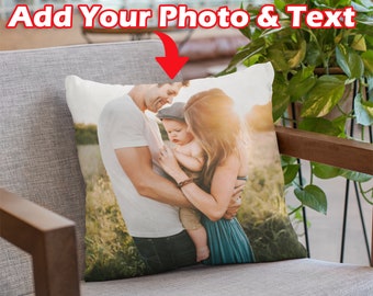 May include: A white cushion with a printed image of a family of three in a field. The family consists of a man, a woman, and a young child. The man is wearing a white t-shirt and jeans. The woman is wearing a blue dress. The child is wearing a white shirt and blue jeans. The image is in a warm, natural light.