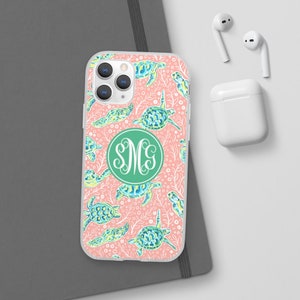 May include: A clear phone case with a pink background and a pattern of green and blue sea turtles. The case has a green circle with the monogram "SMC" in white.