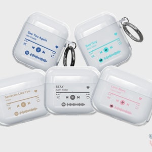 May include: Five clear plastic cases for AirPods with different song titles and artist names printed on them. The cases are all white and have a black ring attached to them. The song titles are "See You Again", "Bad Guy", "Someone Like You", "STAY", and "Love Story".