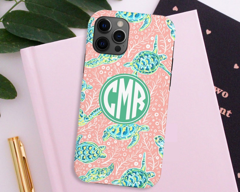 May include: A pink phone case with a white and green sea turtle pattern. The case has a green monogram "CMR" in the center.
