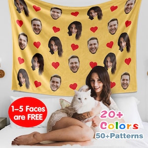 Puede incluir: Una manta de forro polar amarilla con corazones rojos y varias caras impresas en ella. La manta está en una cama con un gato blanco y una persona sentada en ella. El texto en la manta dice "1-5 Faces are FREE, 20+ Colors, 50+ Patterns".