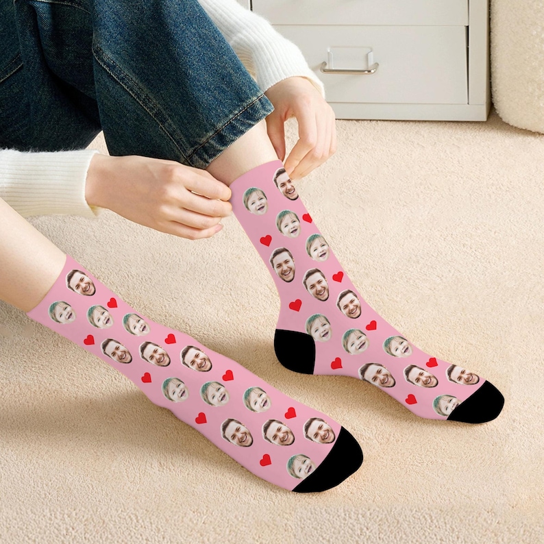 May include: Pink socks with a pattern of red hearts and faces. The faces are of a person, and the socks are shown being worn by a person.
