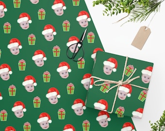 May include: Green wrapping paper with a repeating pattern of a baby wearing a Santa hat and a red gift box.