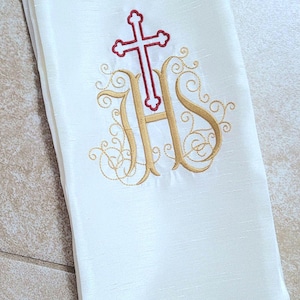 May include: White fabric with a gold embroidered monogram of "IHS" with a red cross above the letters.