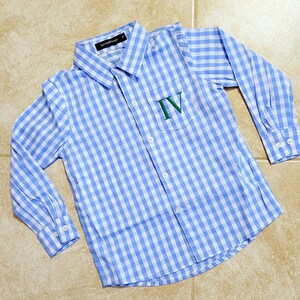 May include: A blue and white gingham button-down shirt with a pocket on the left side. The pocket has the Roman numeral "IV" embroidered on it in green thread.