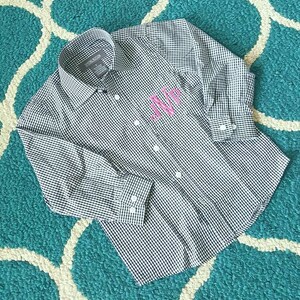 May include: A black and white gingham button-down shirt with long sleeves and a pink monogram on the pocket.