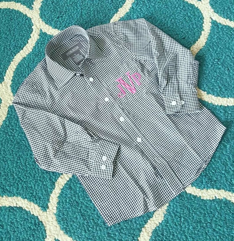 May include: A black and white gingham button-down shirt with long sleeves and a pink monogram on the pocket.