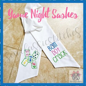 May include: White sash with embroidered game tiles and the words "Bam Dot Crack." The text "Game Night Sashes" is in pink script. A fun accessory for game night.