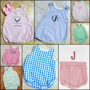 May include: A collection of infant bubble rompers in various gingham and seersucker patterns, featuring embroidered monograms, names, and military-themed text. The garments include sleeveless designs with button closures and elasticized leg openings.