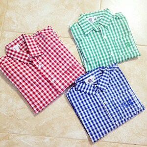May include: Three gingham button-down shirts in red, green, and blue with white checks. Each shirt has a pocket on the left side with a monogram embroidered on it.