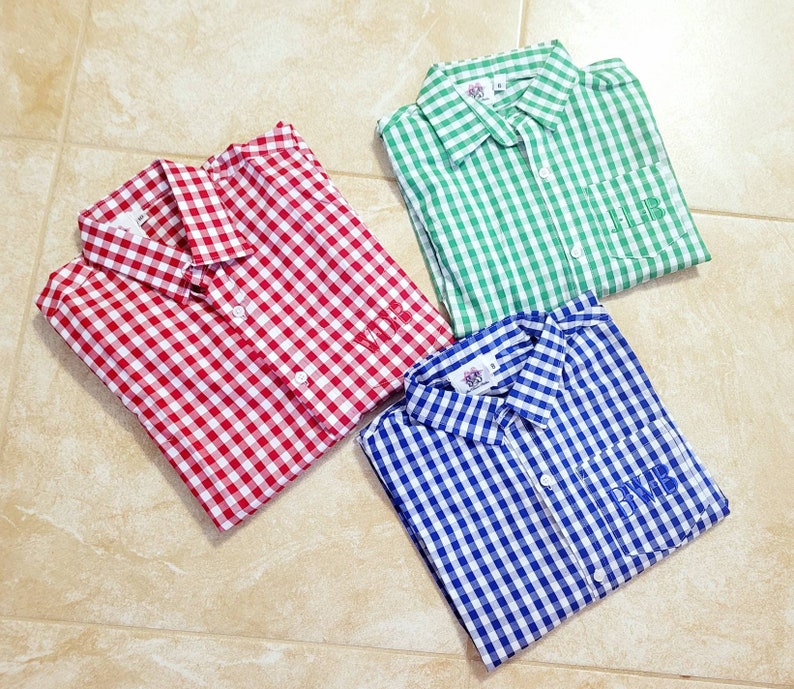 May include: Three gingham button-down shirts in red, green, and blue with white checks. Each shirt has a pocket on the left side with a monogram embroidered on it.
