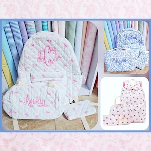 May include: A quilted white backpack, lunch bag, and pencil case set featuring a pink bow pattern and the embroidered name Rowan. Additional sets include a blue floral backpack and lunch bag with the name Virginia, and a white backpack set with black bows.