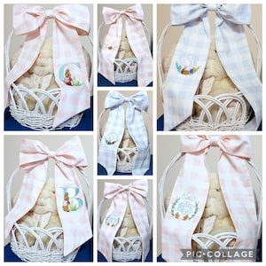 May include: White wicker Easter baskets with plush bunnies, adorned with large gingham bows in pink and blue. Some bows feature embroidered initials, bunnies, and Easter eggs. A charming and festive gift.