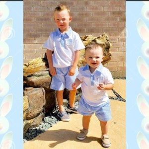 May include: Two young children wearing matching outfits. Each child is wearing a white polo shirt with a blue checkered collar and pocket, paired with blue checkered shorts. The children are standing outside on a sunny day.