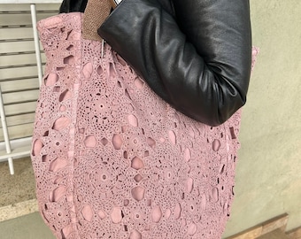May include: A large, pink crocheted tote bag with a brown canvas strap. The bag is made with a delicate, openwork pattern.