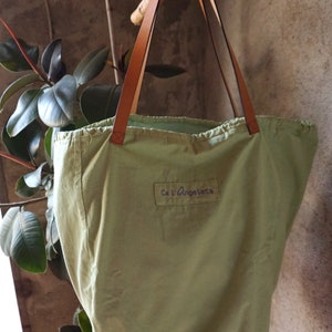 May include: A green canvas tote bag with brown leather straps and the text "Ca l'Angeleta" printed on the front.