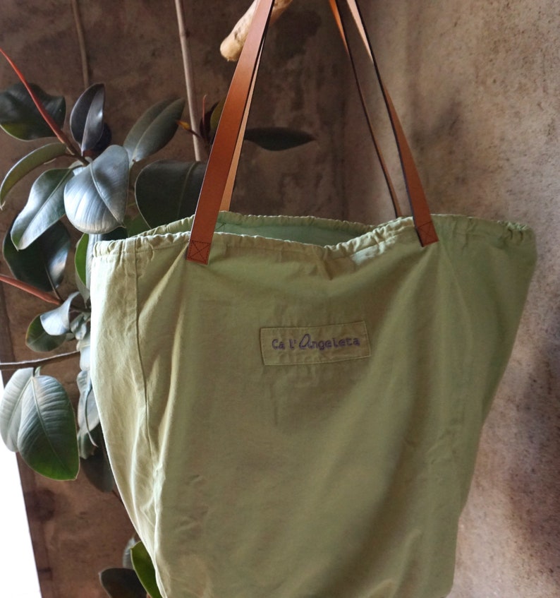 May include: A green canvas tote bag with brown leather straps and the text "Ca l'Angeleta" printed on the front.