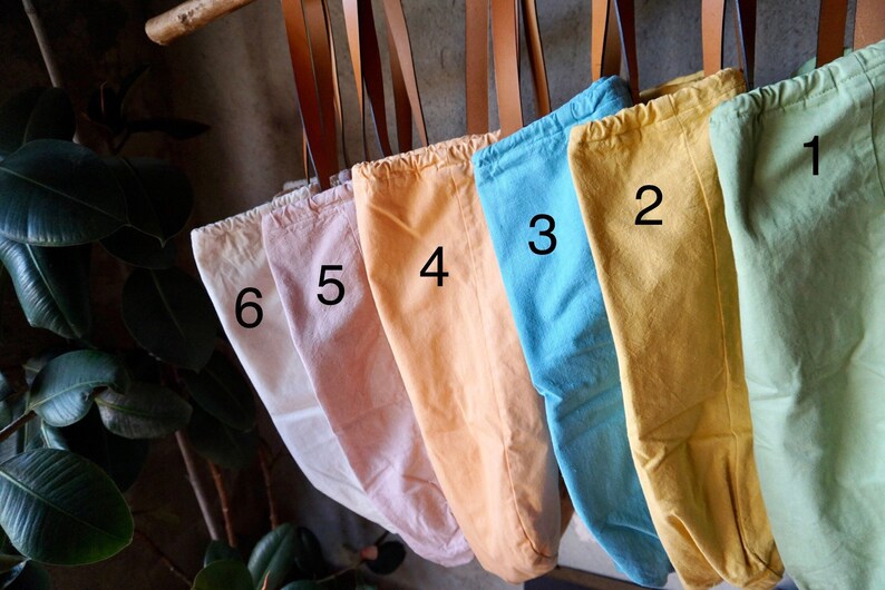 May include: Six canvas tote bags hanging from hooks, each dyed a different pastel color. The bags are numbered 1 through 6, with the numbers visible on the front of each bag.