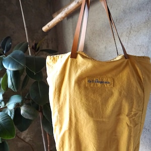 May include: A yellow canvas tote bag with brown leather straps and the text "Los Angeles" embroidered on the front.