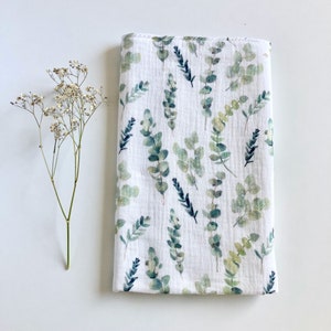 May include: A white muslin swaddle blanket with a green and blue eucalyptus leaf pattern.
