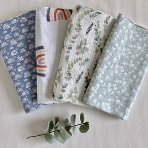 May include: Four different muslin swaddles with various patterns. The swaddles are made of soft, breathable fabric and are perfect for keeping babies warm and comfortable. The patterns include a blue and white rainbow design, a white and brown rainbow design, a green and white eucalyptus design, and a light blue and white floral design.