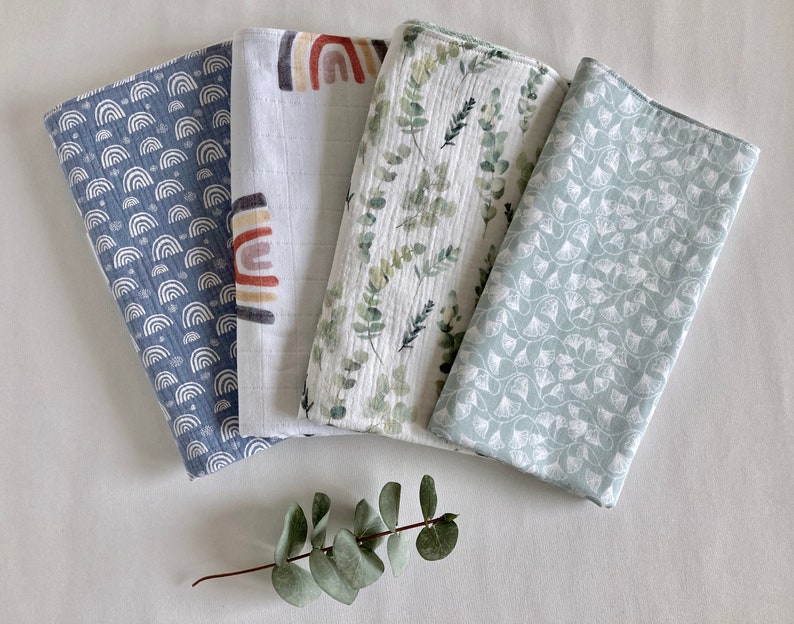 May include: Four different muslin swaddles with various patterns. The swaddles are made of soft, breathable fabric and are perfect for keeping babies warm and comfortable. The patterns include a blue and white rainbow design, a white and brown rainbow design, a green and white eucalyptus design, and a light blue and white floral design.