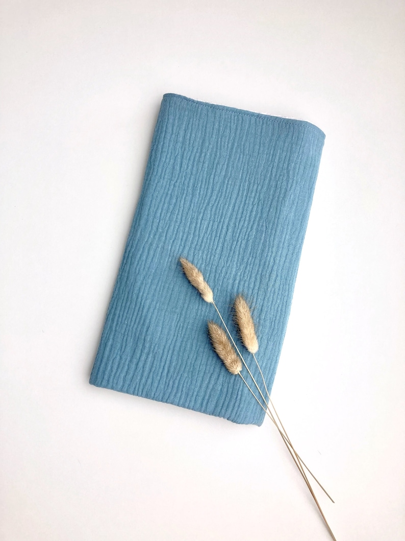 May include: A light blue fabric swatch with a textured surface. Three dried grass stems are placed on top of the fabric.