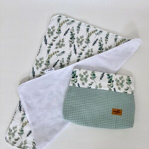 May include: A white muslin baby burp cloth with a green leafy print and a matching green waffle weave pouch with a brown label that says "amilla".