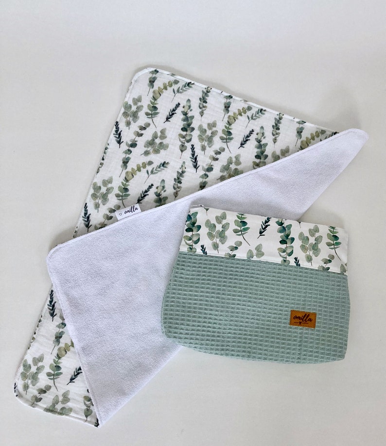 May include: A white muslin baby burp cloth with a green leafy print and a matching green waffle weave pouch with a brown label that says "amilla".