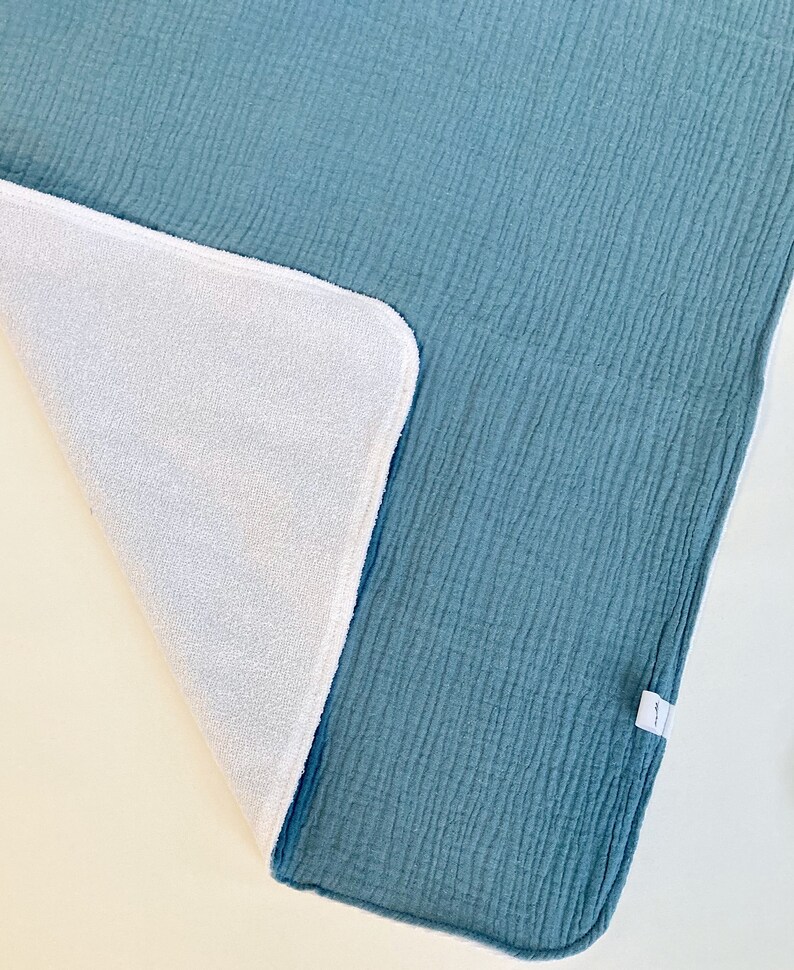 May include: A soft, blue and white reversible baby blanket. One side is a textured blue fabric and the other side is a white terry cloth.