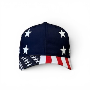 May include: A navy blue baseball cap featuring a pattern of white stars on the crown. The curved brim displays a graphic print of the American flag, showcasing a section of white stars on a blue field on the left and red and white vertical stripes.