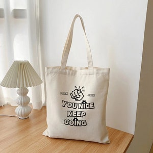 May include: A white canvas tote bag with black text and a pointing hand graphic. The text reads "You Nice Keep Going" with "Park" and "Jimin" written above and below the hand.