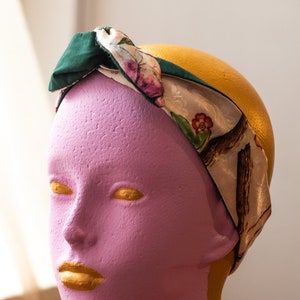 May include: A pink mannequin head with gold painted lips and eyes wearing a green and white floral patterned headband.