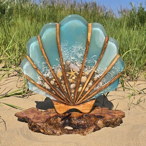 Könnte beinhalten: Dekorative Muschelbildhauerei mit hellblauem Harzoberteil und Holzakzenten. Das Muscheldesign zeigt eine Strandszene mit Sand, Muscheln und einem Seestern. Die Skulptur ist auf einem Holzsockel montiert.