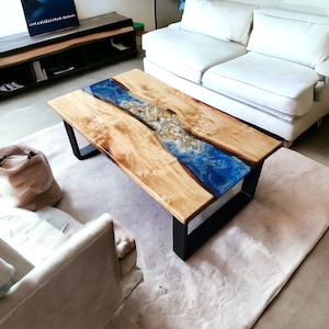 Könnte beinhalten: Ein Holz-Couchtisch mit einem blauen und weißen Epoxidharz-Flussdesign. Das Harz enthält kleine weiße Steine und Muscheln. Der Tisch hat einen schwarzen Metallrahmen.