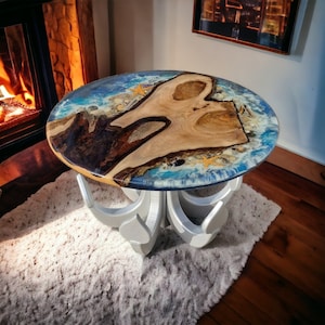 Könnte beinhalten: Ein runder Holztisch mit einer blauen, weißen und braunen Epoxidharzplatte. Der Tisch hat ein einzigartiges, silbernes, dekoratives Gestell mit wellenförmigem Design.