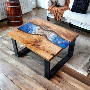 May include: A wooden coffee table with a blue and white epoxy river design. The river design features white swirls and small white stones. The table has a black metal frame.