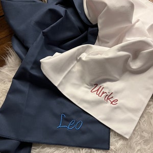 May include: Two personalized towels, one navy blue with the name "Leo" embroidered in blue thread, and one white with the name "Ulrike" embroidered in red thread.