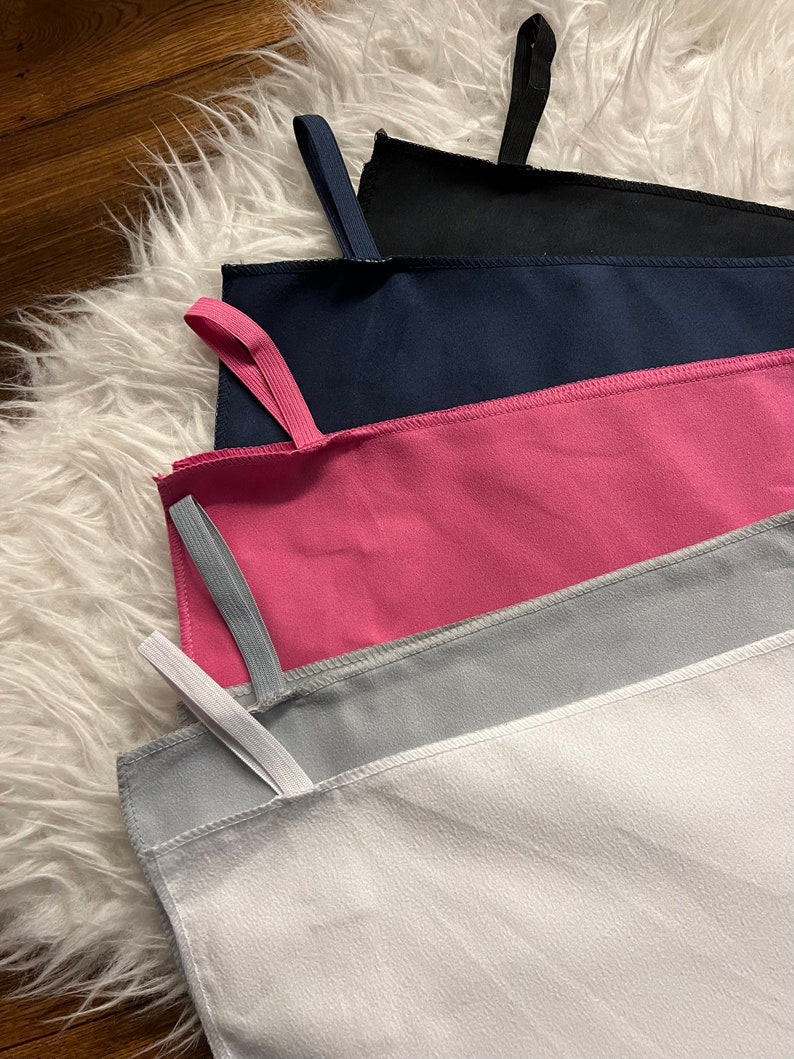 May include: Five microfiber towels in different colors, stacked on top of each other. The towels are white, gray, pink, navy blue, and black. Each towel has a loop at the top for hanging.
