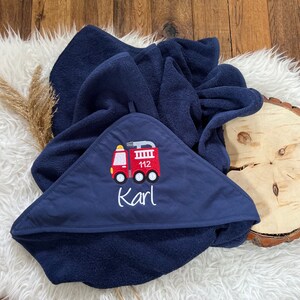 May include: A navy blue hooded towel with a red fire truck embroidered on the front. The fire truck has the number 112 on the side and the name "Karl" is embroidered below it.