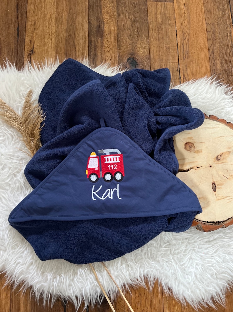 May include: A navy blue hooded towel with a red fire truck embroidered on the front. The fire truck has the number 112 on the side and the name "Karl" is embroidered below it.