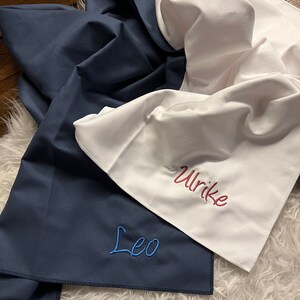 May include: Two personalized towels, one navy blue with the name "Leo" embroidered in blue thread, and one white with the name "Ulrike" embroidered in red thread.