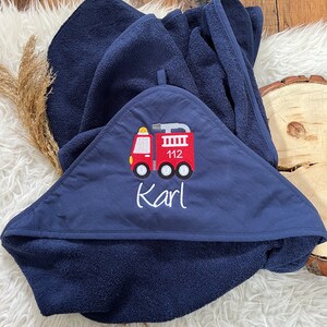May include: A navy blue hooded towel with a red fire truck embroidered on the front. The fire truck has the number 112 on the side and the name "Karl" is embroidered below it.