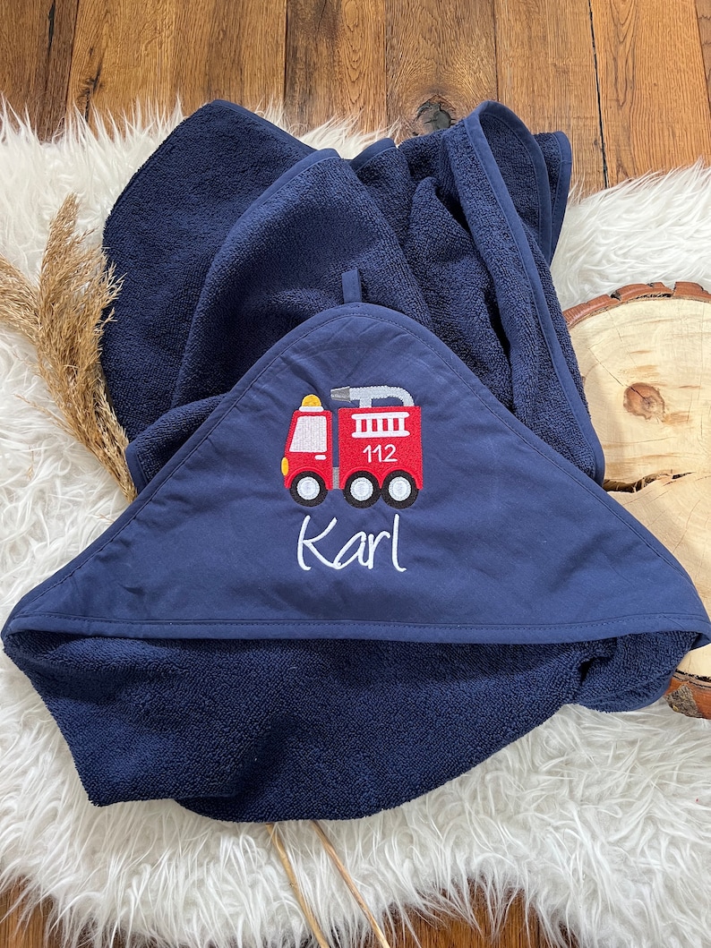 May include: A navy blue hooded towel with a red fire truck embroidered on the front. The fire truck has the number 112 on the side and the name "Karl" is embroidered below it.