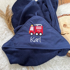 May include: A navy blue hooded towel with a red fire truck embroidered on the front. The fire truck has the number 112 on the side and the name "Karl" is embroidered below it.