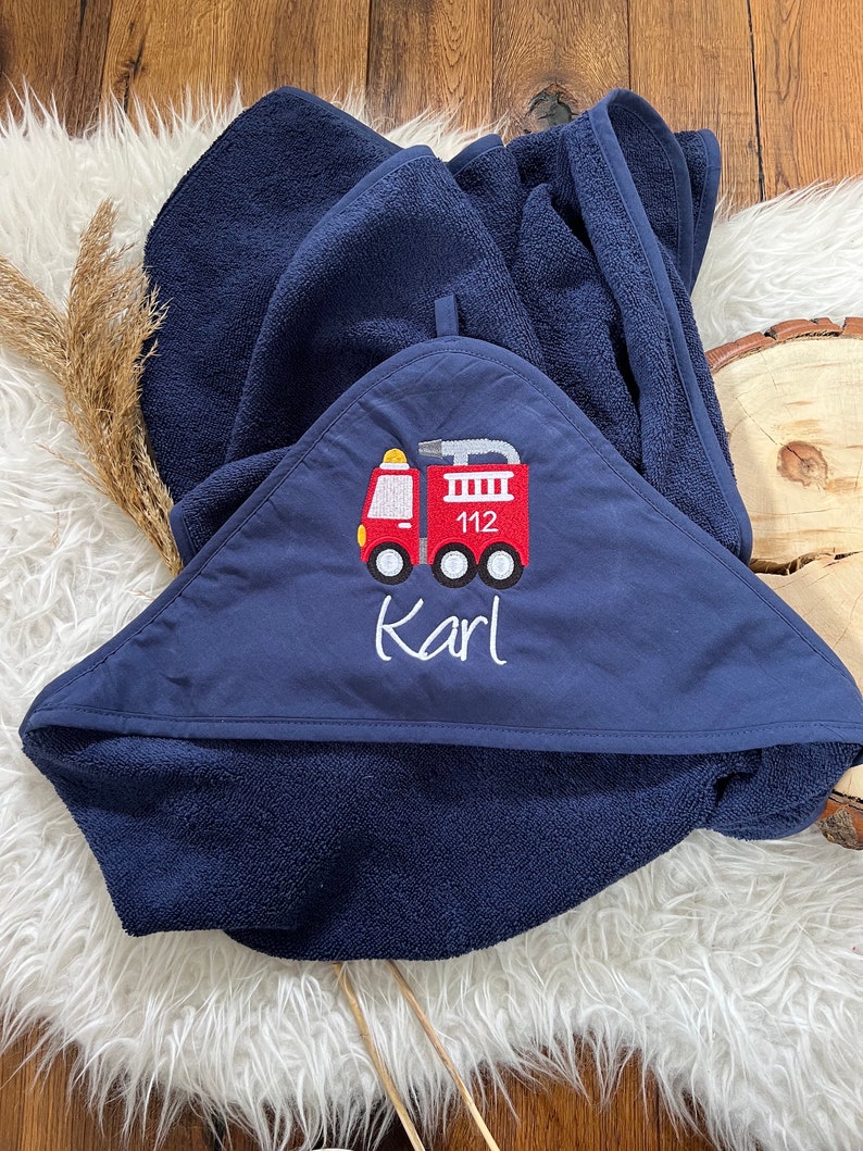 May include: A navy blue hooded towel with a red fire truck embroidered on the front. The fire truck has the number 112 on the side and the name "Karl" is embroidered below it.