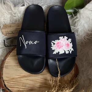 May include: A pair of black slides with a floral design on one slide and the word "Nono" on the other slide.
