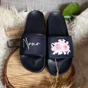 May include: Pair of black slide sandals with embroidered floral designs. One sandal has the word "Nono" embroidered on it.